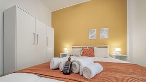 A hotel room with a bed, two bedside tables with lamps, a wardrobe, and artwork on the wall. - [Sea Side] Beach 2 min • Free WiFi • Smart TV (Savona)