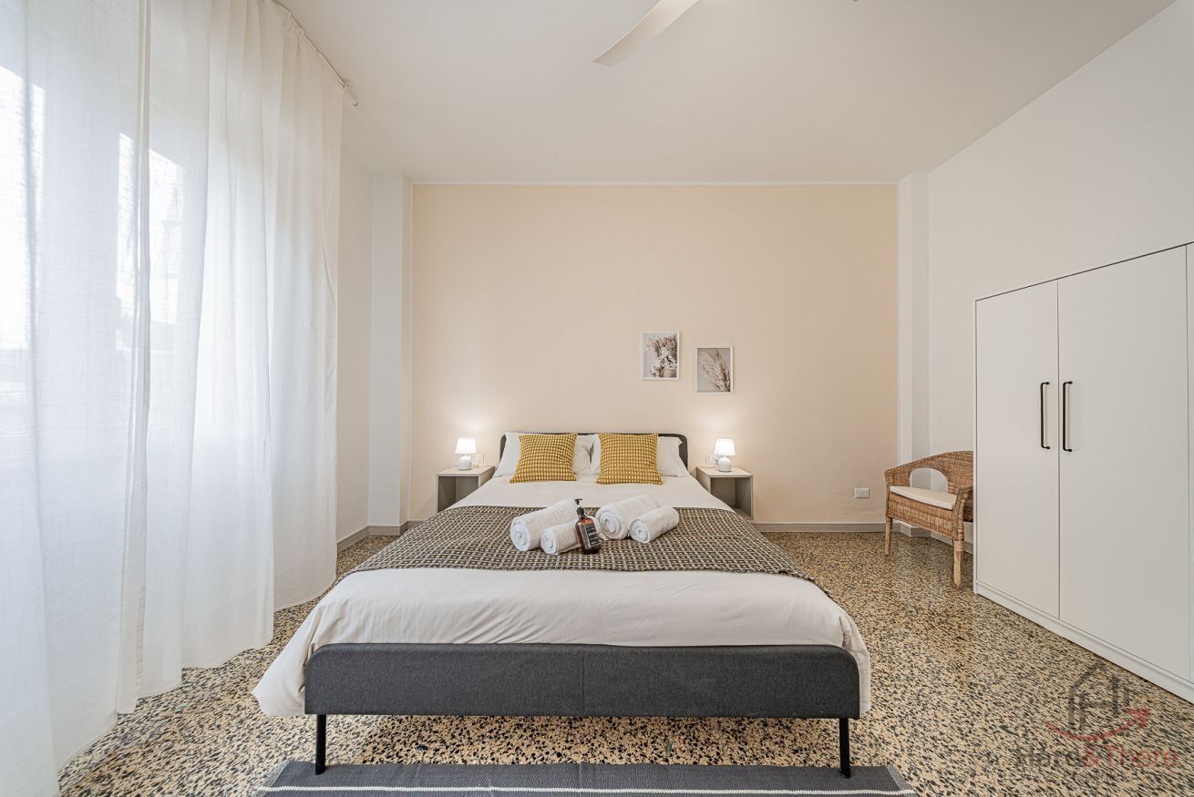 Une chambre à coucher avec un lit, des tables de chevet, une armoire et une fenêtre avec des rideaux.