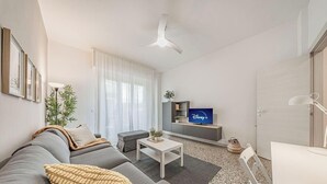 A modern living room with a sofa, coffee table, TV, and a ceiling fan. - [Sea Side] Beach 2 min • Free WiFi • Smart TV (Savona)
