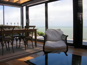 Une pièce moderne avec une table et des chaises en verre, un fauteuil confortable et une vue sur la mer.