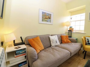 A living room with a sofa, pillows, a lamp, a bookshelf, and a window with a view. - Lightkeepers Fold (Eyemouth)
