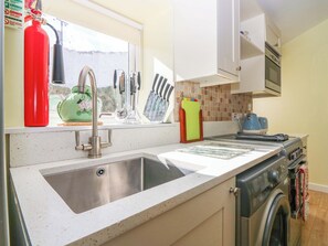 A kitchen with a stainless steel sink, a red fire extinguisher, a green kettle, and a washing machine. - Lightkeepers Fold (Eyemouth)