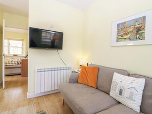 Ein Wohnzimmer mit einer Couch, einem an der Wand montierten Fernseher, einer Heizung und einem gerahmten Gemälde.