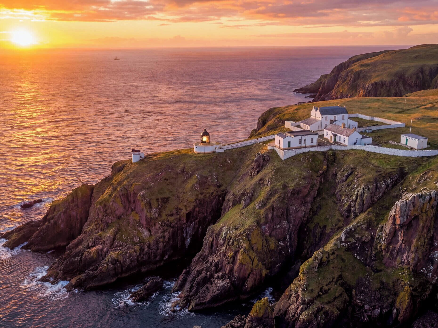 Un ensemble de bâtiments situé sur la côte, comprenant un phare, des structures blanches et offrant une vue sur la mer au coucher du soleil.