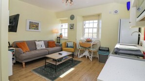 A compact living space with a sofa, coffee table, dining table, and chairs. - Lightkeepers Fold (Eyemouth)
