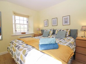 A bedroom with a bed, a window, a bedside table, a lamp, and framed pictures on the wall. - Lightkeepers Fold (Eyemouth)