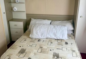Una cama con una colcha estampada, una mesita de noche con cajones y un estante con objetos decorativos.