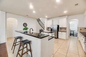 A modern kitchen with a central island, white cabinetry, and a staircase leading to another level. - FS714 - Near The Star - Sleeps 8 - Parking - FS714 (Frisco)