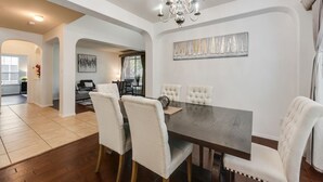 Zona pranzo con tavolo in legno scuro, sedie imbottite bianche e un lampadario.