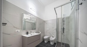 Un bany modern amb un box de dutxa de vidre, un lavabo amb mirall i dues vàteres.