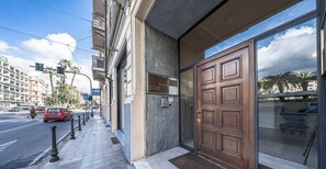 Entrada d'hotel amb una porta de fusta gran, un vestíbul de vidre i una vorera amb protectors.