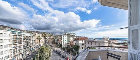Ein Balkon mit freiem Blick auf eine Küstenstraße, Gebäude und ein weiter Schiffshorizont.