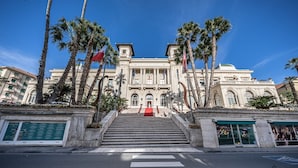 A grand building with a central entrance, flanked by palm trees and flags, leading up to a red carpet. - [Stunning Residence] Marina & City view • A/C (Sanremo)