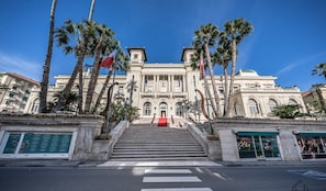 A grand building with a central entrance, flanked by palm trees and flags, leading up to a red carpet. - [Stunning Residence] Marina & City view • A/C (Sanremo)