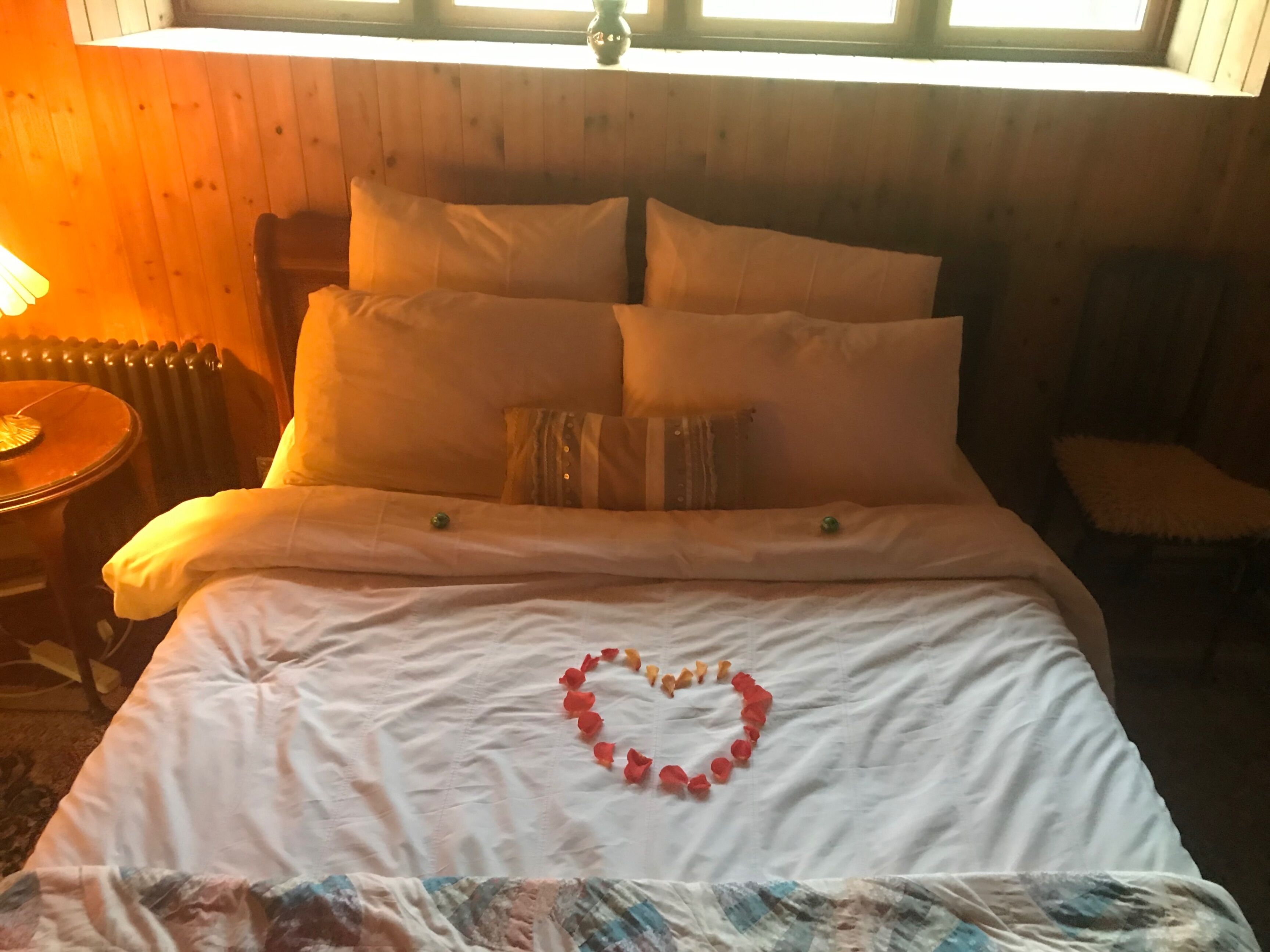 Una cama con un adorno con forma de corazón, un cabecero de madera, un radiador, una lámpara y una silla.