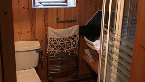 Un interior de madera con un inodoro, una ventana pequeña y una zona de ducha.