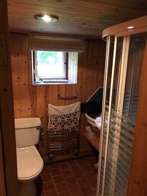 Un interior de madera con un inodoro, una ventana pequeña y una zona de ducha.