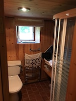 A wooden interior with a toilet, a small window, and a shower area.