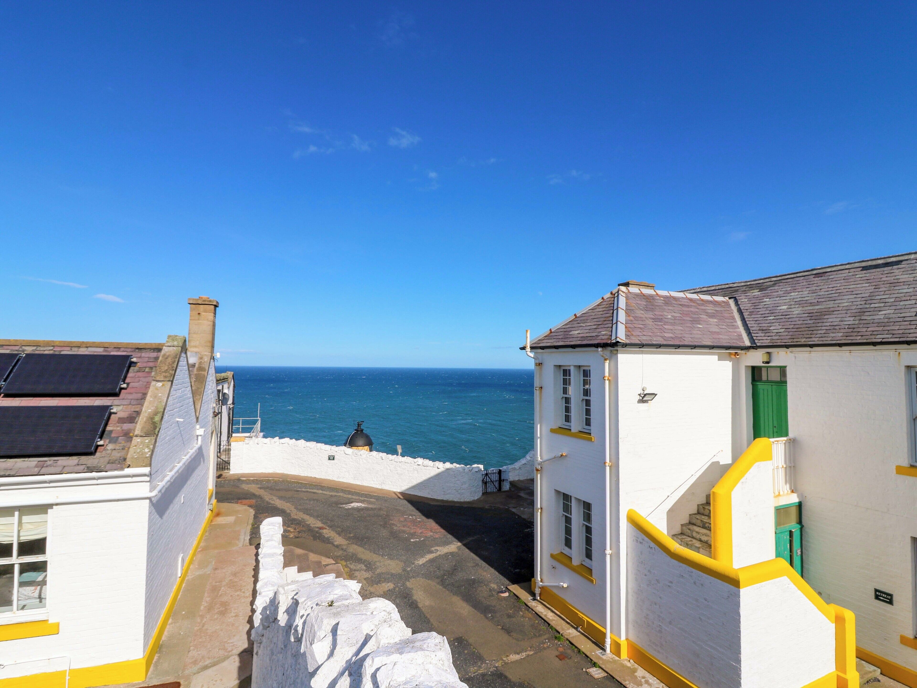 Un bâtiment situé sur la côte, doté d’une façade blanche, de bordures jaunes et d’un escalier menant à un niveau supérieur.