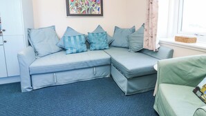 A room with a light blue sofa, a green armchair, a framed painting, a window with curtains, and a white cabinet. - Lightkeepers Flaghouse (Eyemouth)