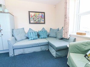 A room with a light blue sofa, a green armchair, a framed painting, a window with curtains, and a white cabinet. - Lightkeepers Flaghouse (Eyemouth)