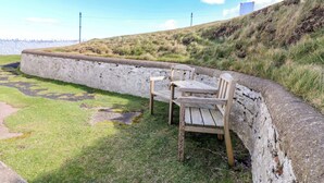 A coastal area with a low stone wall, two wooden chairs, and a grassy path. - Lightkeepers Flaghouse (Eyemouth)