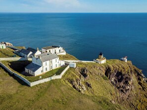 A coastal village with white buildings, a lighthouse, and a stone wall. - Lightkeepers Flaghouse (Eyemouth)
