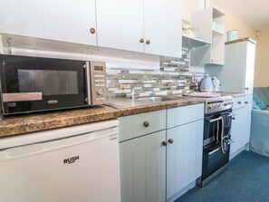 A compact kitchen with a microwave, sink, stove, and dishwasher. - Lightkeepers Flaghouse (Eyemouth)