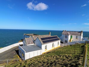 A coastal building with solar panels, a grassy area, and a view of the sea. - Lightkeepers Flaghouse (Eyemouth)