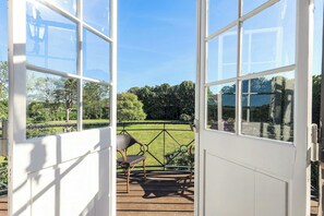 A view through a glass door with a wooden deck, a wicker chair, and a green lawn.