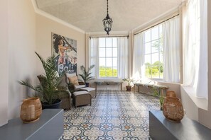 A sunlit room with a patterned floor, wicker furniture, and a large window with curtains.