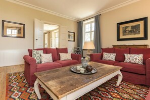 Un salon avec deux canapés rouges, une table basse en bois, des tapis à motifs et des tableaux encadrés accrochés aux murs.