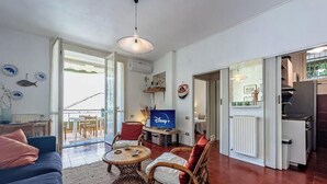 A living room with a sofa, chairs, a TV, and a balcony.