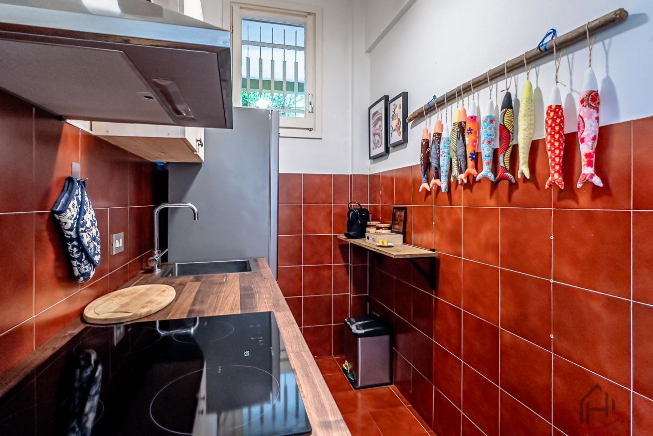 A kitchen with a wooden countertop, a built-in stove, a hanging rack with kitchen utensils, and a window with bars.