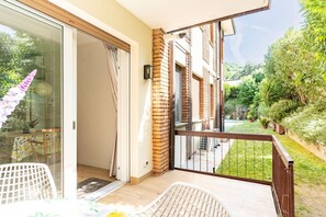 Ein Balkon mit Blick auf einen Garten, eine Glastür und ein weißer Stuhl.
