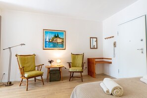 Ein Hotelzimmer mit einem Bett, zwei Stühlen, einem kleinen Tisch mit einer Lampe, einem Gemälde und einem Holzschrank.