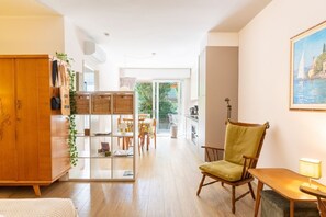 Ein modernes Wohnzimmer mit einer Holzkabine, einem grünen Sessel, einem Essbereich mit Tisch und Stühlen sowie Blick durch eine Glastür nach draußen.