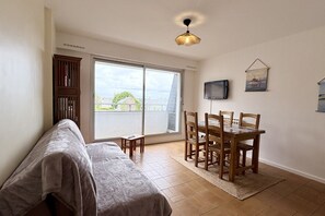A room with a bed, a dining table with chairs, a TV on the wall, and a large window. - Getaway with an ocean view, balcony, and parking (Le Crotoy)