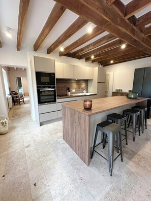 Une cuisine moderne avec un îlot central, des tabourets de bar et un coin repas à l’arrière-plan.