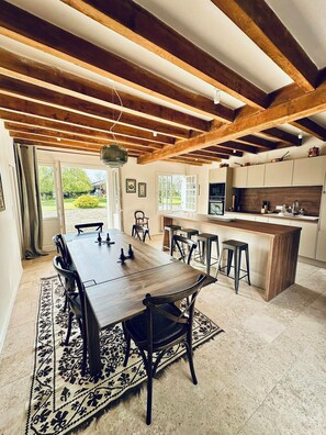Un espace repas avec une table et des chaises en bois, une cuisine équipée d’appareils modernes et une vue sur l’extérieur.