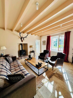 Un salon comprenant un canapé, des fauteuils, une table basse, une cheminée et une grande fenêtre avec des rideaux.