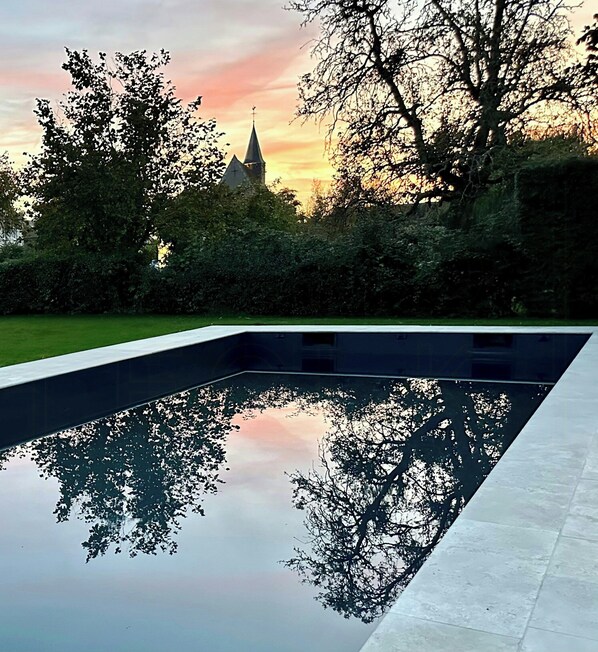 Une piscine dont l’eau reflète clairement les arbres et, au loin, le clocher d’une église.