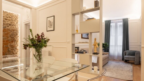 A modern living room with a glass table, white chairs, a stone wall, a bookshelf, and a grey sofa. - A cozy and charming home featuring beautiful stone details, bright interiors, and a modern, relaxing atmosphere. Conveniently located in a central area, Atipico Apartment is perfect for guests who want to experience Florence with style and comfort.✔ Pe (Firenze)
