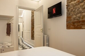 Ein Hotelzimmer mit Bett, einem an der Wand befestigten Fernseher, einer Steinwand, einem Flur mit Schachbrettmuster und einer Tür zu einem weiteren Raum.