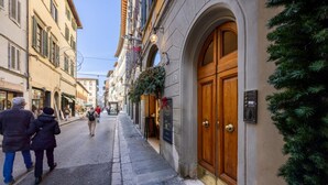 A narrow street with buildings on either side, a wooden door with a plaque, and a Christmas tree on the right. - A cozy and charming home featuring beautiful stone details, bright interiors, and a modern, relaxing atmosphere. Conveniently located in a central area, Atipico Apartment is perfect for guests who want to experience Florence with style and comfort.✔ Pe (Firenze)