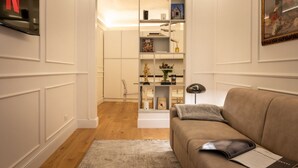 A living room with a beige sofa, a bookshelf, and a TV mounted on the wall. - A cozy and charming home featuring beautiful stone details, bright interiors, and a modern, relaxing atmosphere. Conveniently located in a central area, Atipico Apartment is perfect for guests who want to experience Florence with style and comfort.✔ Pe (Firenze)