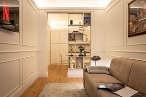 Ein Wohnzimmer mit einem beigen Sofa, einem Bücherregal und einem an der Wand befestigten Fernseher.