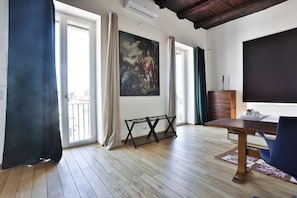Ein Zimmer mit Holzboden, einem Esstisch, einem Stuhl, einem Bild an der Wand und einem Fenster mit Vorhängen.