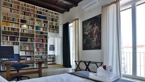 Um quarto com uma grande estante de livros, um quadro, uma cama e uma escrivaninha.