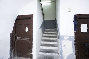 Eine Treppe mit Handlauf, eine braune Tür und eine Wand mit abblätternder Farbe.